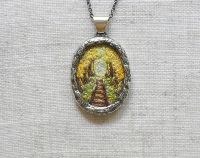 Pendentif avec un chemin de fer brodé de couleur jaune fabriqué par Rosalie Lambert-Sarrazin.