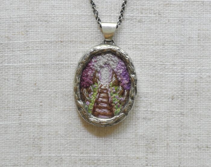 Pendentif avec un chemin de fer brodé de couleur mauve fabriqué par Rosalie Lambert-Sarrazin.