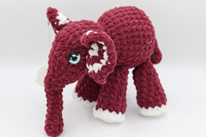 Photo d'une peluche éléphant tricotée à la main en laine rouge avec des détails blancs et des yeux expressifs. Cette peluche est douce et idéale pour les enfants.