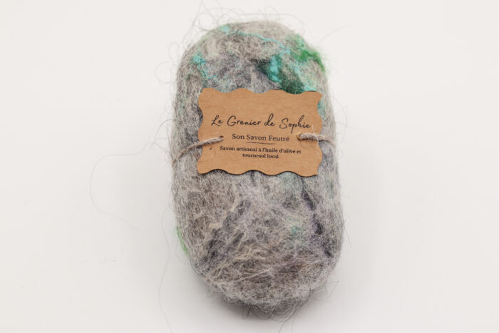 Photo d'un savon feutré artisanal enveloppé dans une fibre naturelle, avec une étiquette indiquant 'Le Grenier de Sophie'. Ce savon est fabriqué à partir d'huile d'olive et de tournesol local.