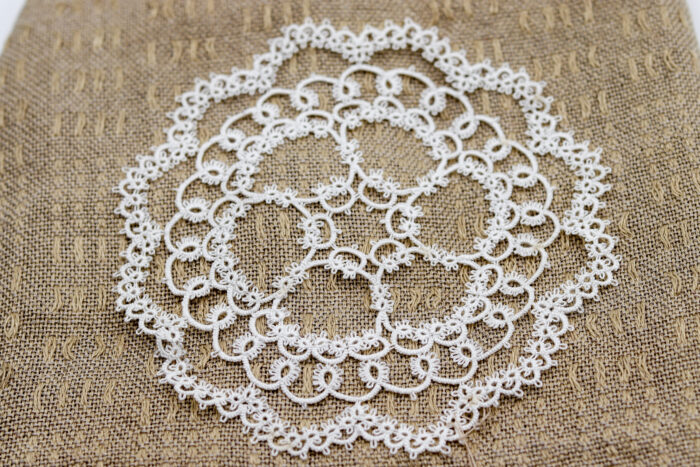 Photo d'un napperon de frivolité blanc, fait à la main avec des motifs délicats en dentelle. Parfait pour ajouter une touche d'élégance à une table ou un meuble.