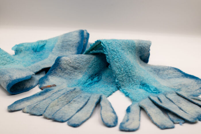 Foulard en feutre turquoise avec des nuances claires et foncées, présentant une texture irrégulière et des bords découpés, posé à plat sur une surface blanche.