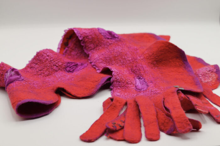 Foulard en feutre rouge et magenta avec une texture irrégulière et des détails en relief, posé à plat sur une surface blanche.